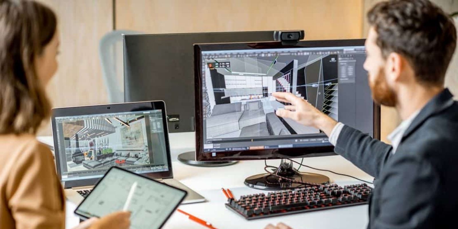 Male pointing at lounge designs on a desktop computer beside a women working on a tablet