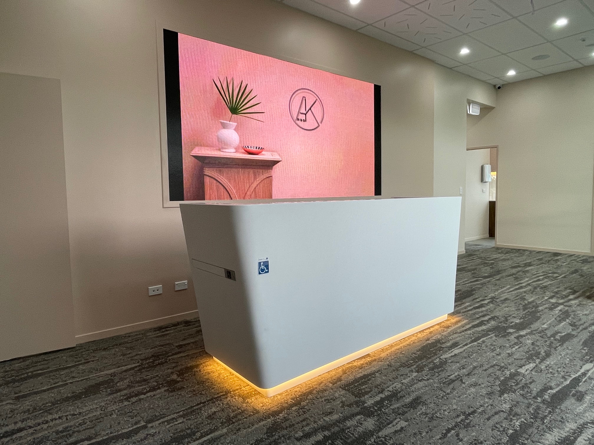 Reception area with white counter in front of a pink photo on the wall of a plant on a desk